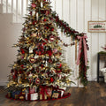 Heavily Decorated Snow Dusted Alpine Christmas Tree with Presents Underneath. Red Color Scheme. Tree In Front of White Staircase. Garland Decorating Railing of Staircase.