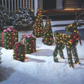NOMA Winter Garden Collection on Snow in front of Partially Visible Porch. Winter Garden Cone Trees, Reindeer and 3-Pack Gift Boxes.