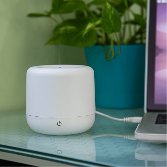 Small humidifier resting on a desk being charged by the USB port of a computer