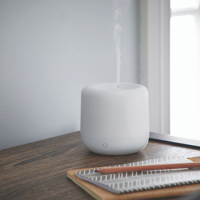 Small humidifier on a wood desk emitting mist into the air
