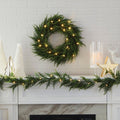 Cedar Wreath Lit Up on White Tiled Wall Background Above Fireplace Mantle. Mantle is Decorated with Cedar Garland and Other Modern Christmas Decor