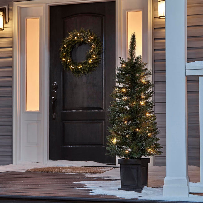 NOMA 4 Ft Farrow Potted Christmas Tree on Porch Entrance infront of Door. Wreath on Door, Snow on Deck/Floor of Porch