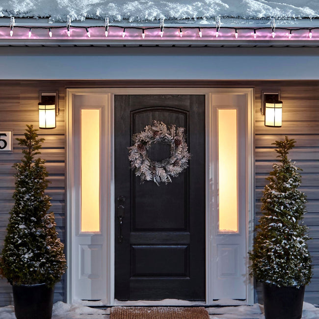 Noma C6 Pink String Lights on a roof edge above home entrance. Wreath on door and two potted trees on porch