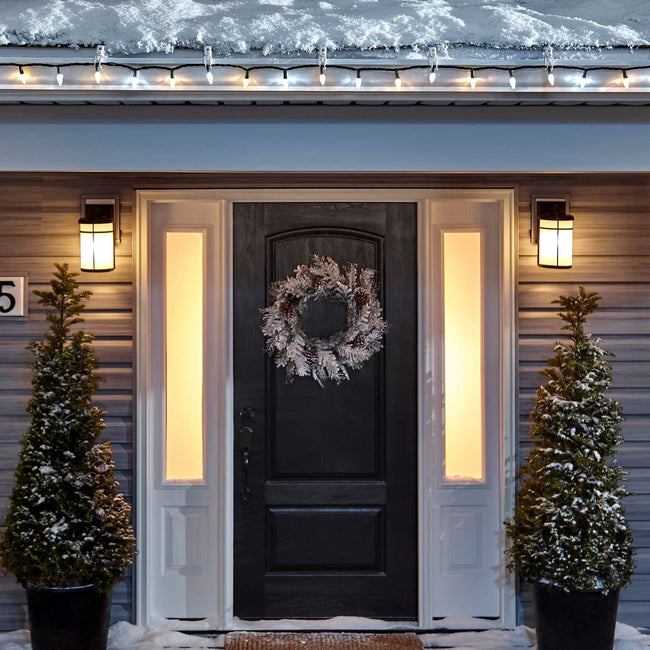 Noma C6 Warm & Pure White String Lights, on a roof edge above home entrance. Wreath on door and two potted trees on porch
