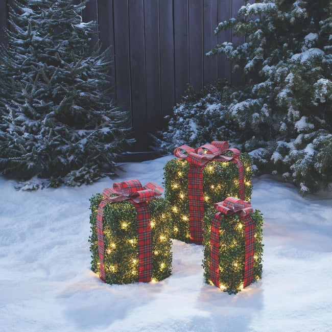 NOMA Incandescent Winter Garden Gift Boxes, 3-Pack - On Snow Covered Lawn. Trees and Wooden Fence in Background.